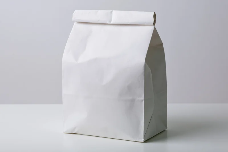 White paper bag standing on a plain surface with folded top sealed
