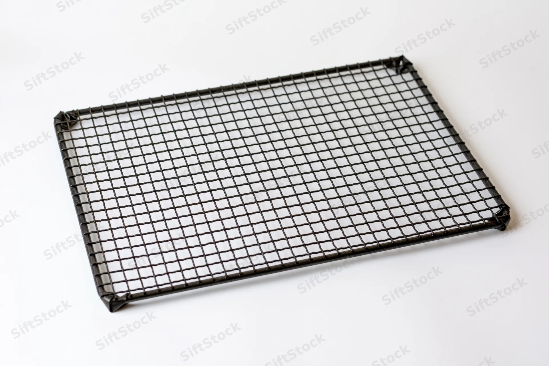 Rectangular dark metal wire cooling rack lying flat on white surface