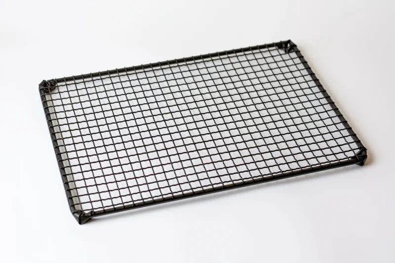 Rectangular dark metal wire cooling rack lying flat on white surface