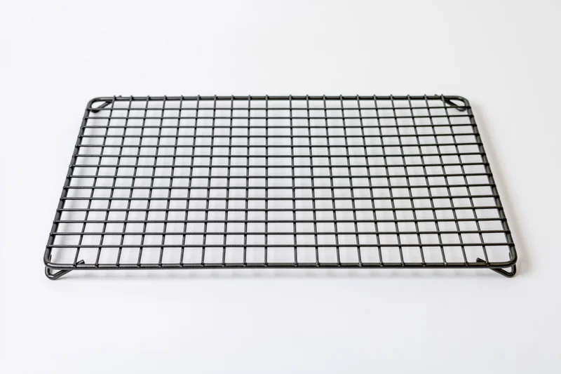 Rectangular dark metal wire cooling rack lying flat on white surface