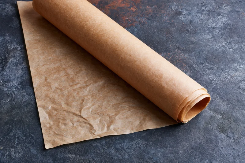 Roll of brown parchment baking paper partially unrolled on dark textured surface