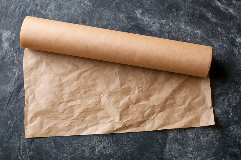 Roll of brown parchment baking paper partially unrolled on dark stone surface