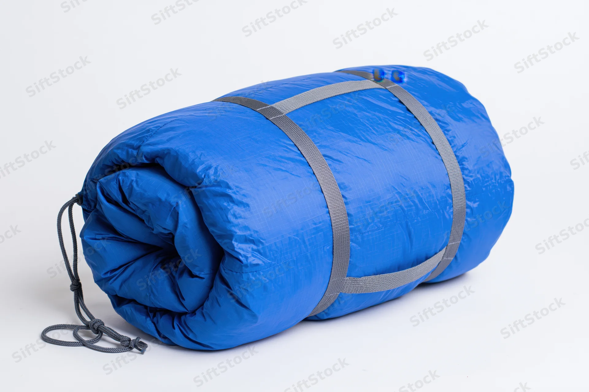 Rolled blue nylon sleeping bag secured with straps and drawstring on white background