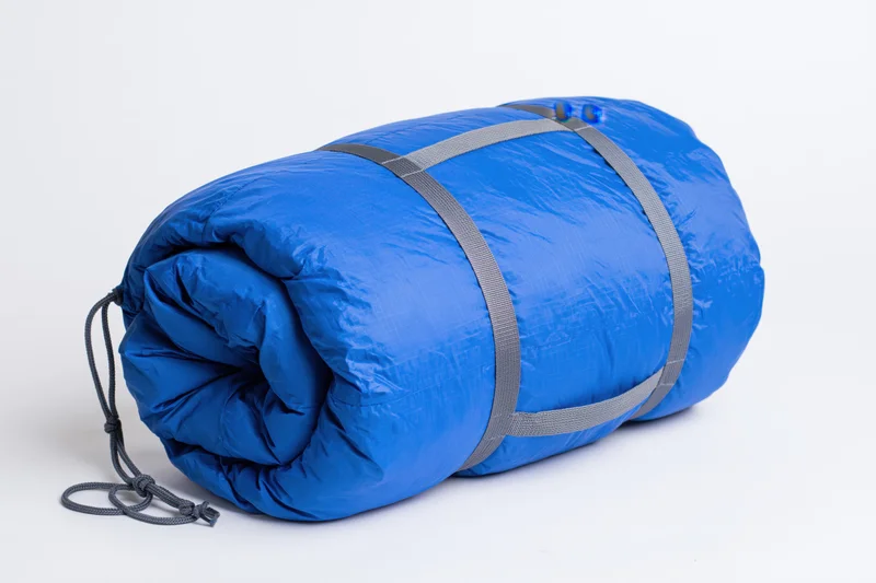 Rolled blue nylon sleeping bag secured with straps and drawstring on white background