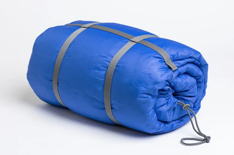 Rolled blue nylon sleeping bag secured with straps on white background