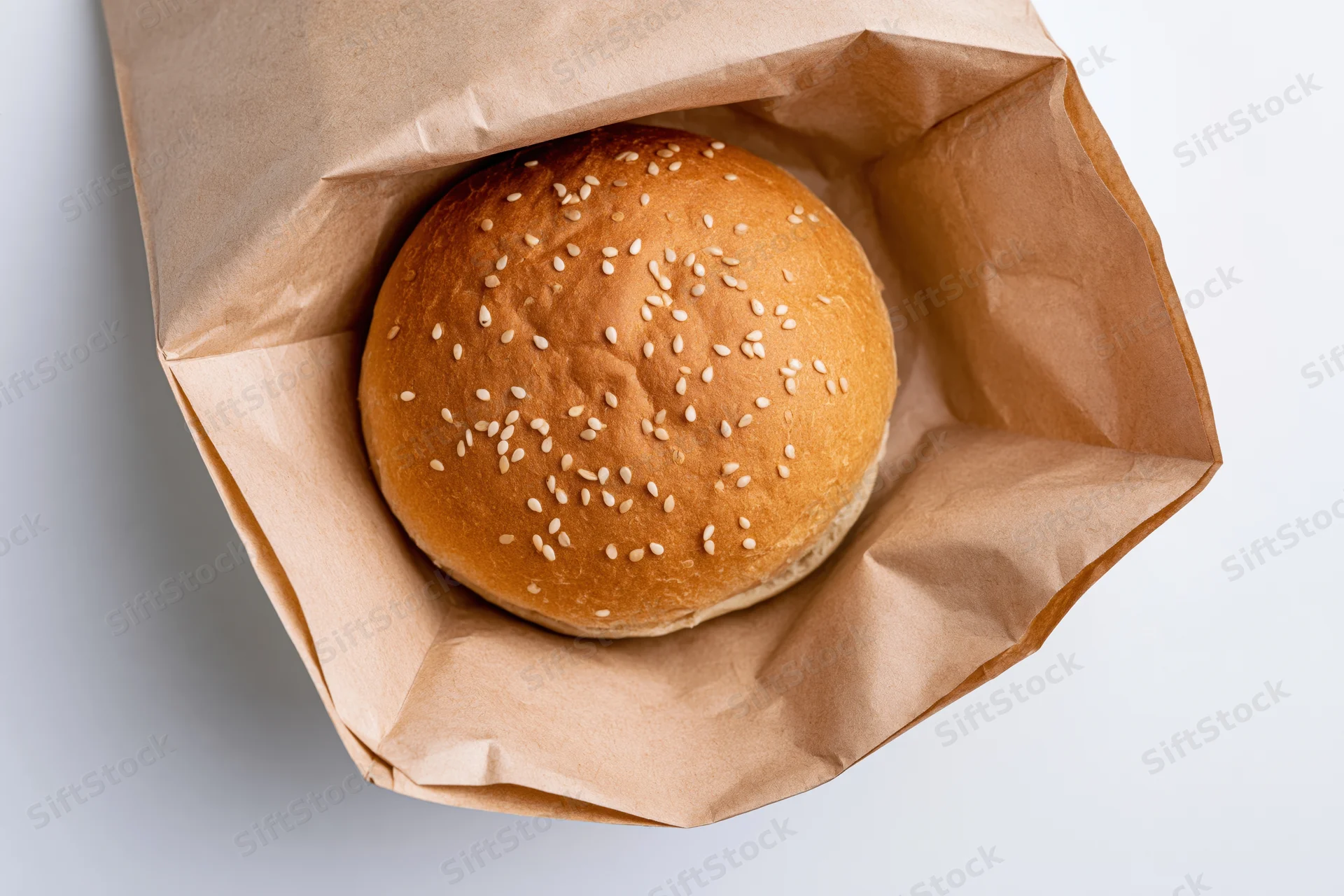 Sesame seed burger bun in open kraft paper bag on white surface