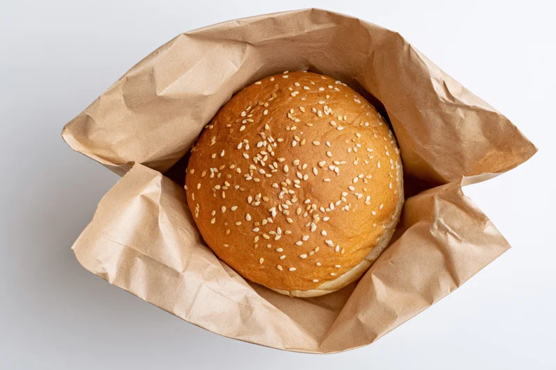 Sesame seed bun in open kraft paper bag on white background