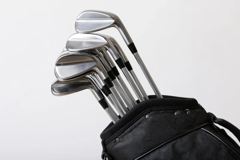 Golf clubs including irons wedges and driver arranged upright in a black golf bag against a white background