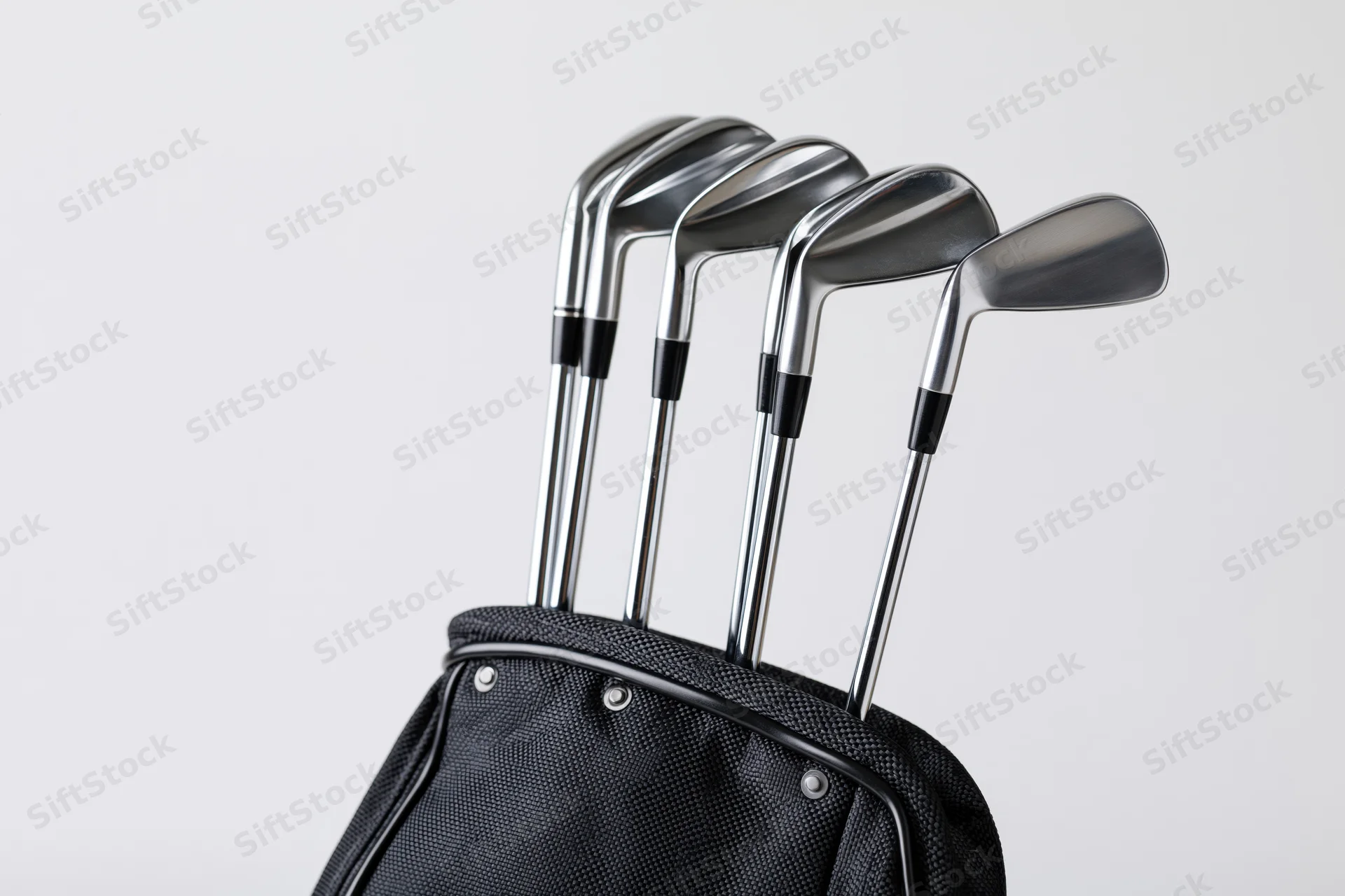 Golf clubs including irons wedges and a driver standing upright in a black golf bag against a white background