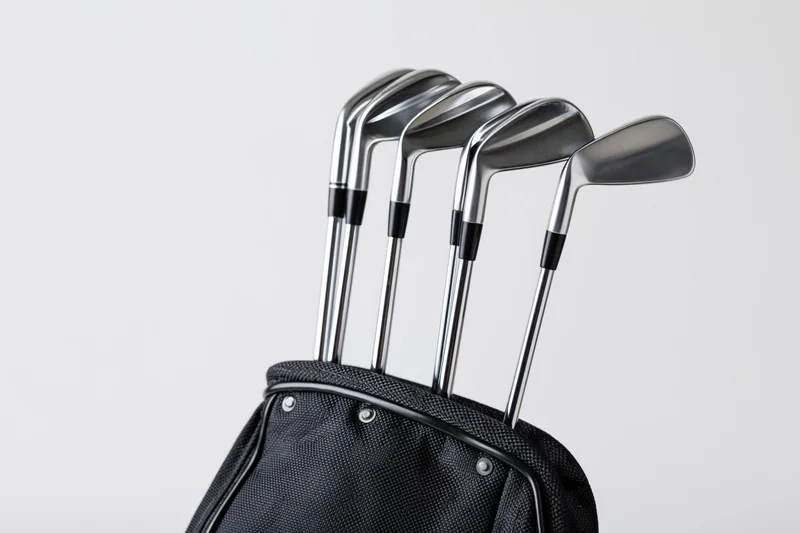 Golf clubs including irons wedges and a driver standing upright in a black golf bag against a white background