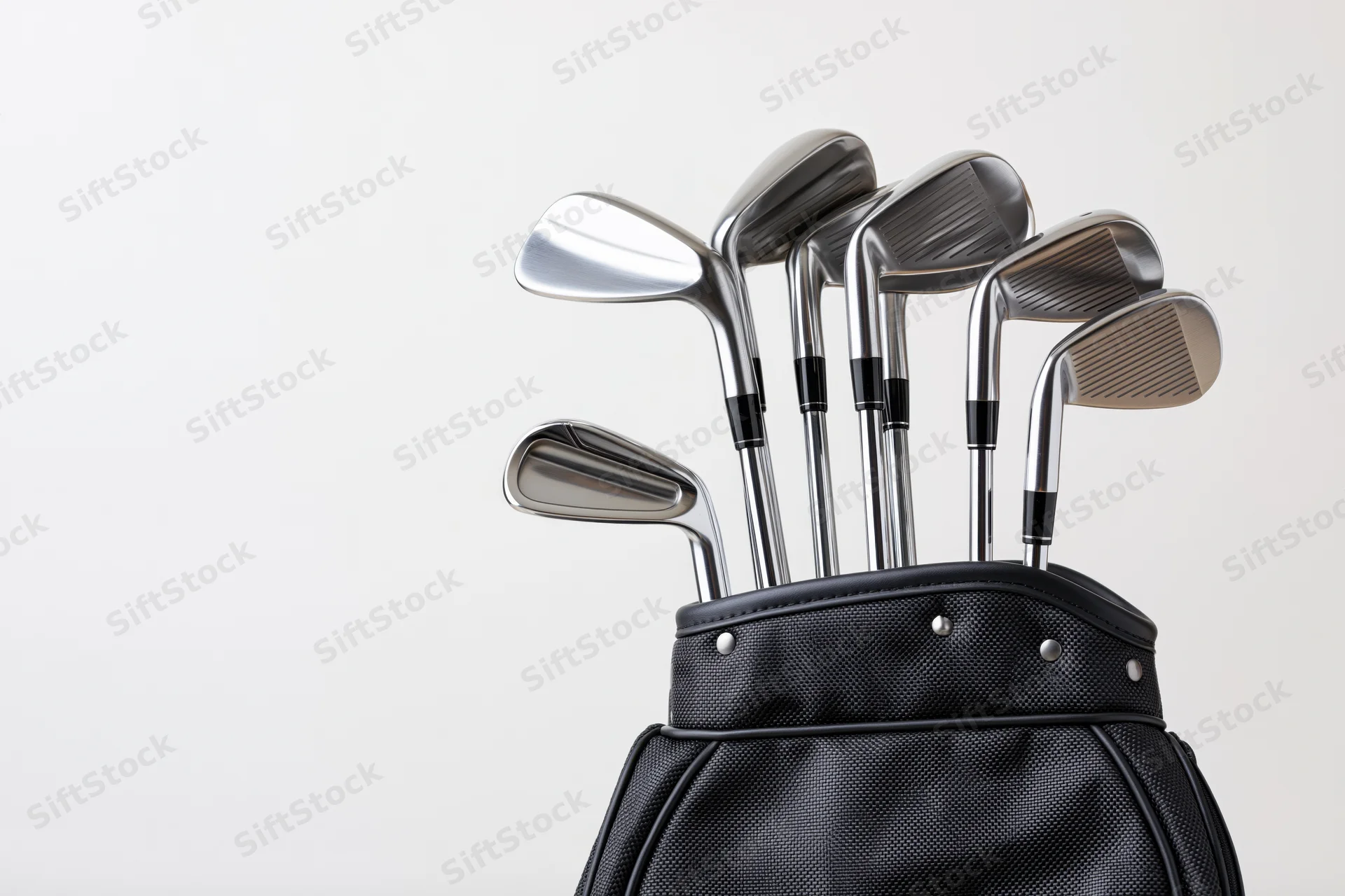 Golf clubs including irons wedges and a driver arranged upright in a black golf bag against a white background