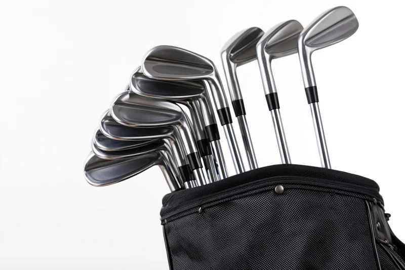 Golf clubs set including irons wedges and driver standing upright in a black golf bag against white background