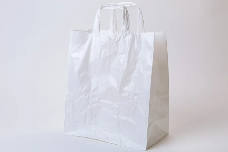 Empty white plastic shopping bag standing upright on plain white surface