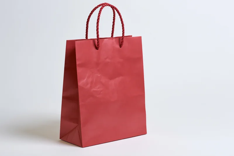 Red glossy paper shopping bag with twisted rope handles on white background