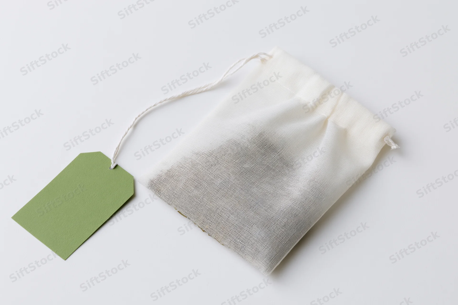 White mesh tea bag with green label tag on plain surface