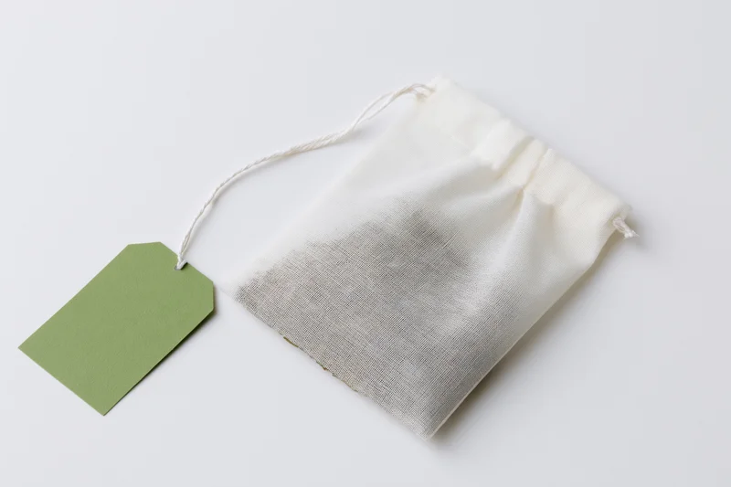 White mesh tea bag with green label tag on plain surface