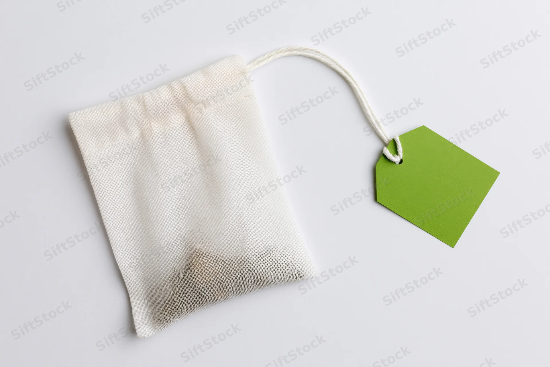 White mesh tea bag with green tag on plain surface