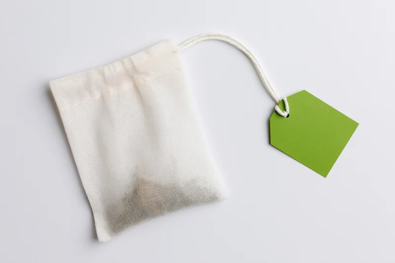 White mesh tea bag with green tag on plain surface