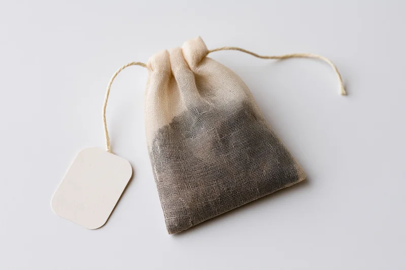 Single tea bag with drawstring and blank paper tag on white background