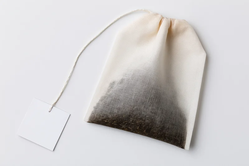Unused tea bag with blank paper tag on white surface