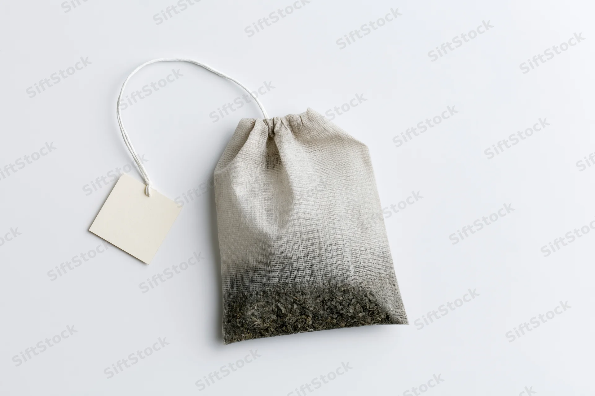 Single unused tea bag with a blank paper tag on white background