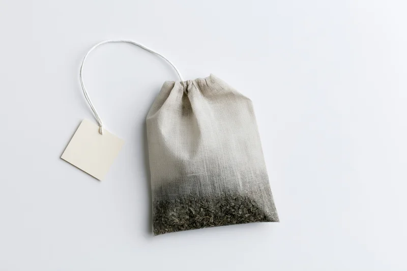 Single unused tea bag with a blank paper tag on white background