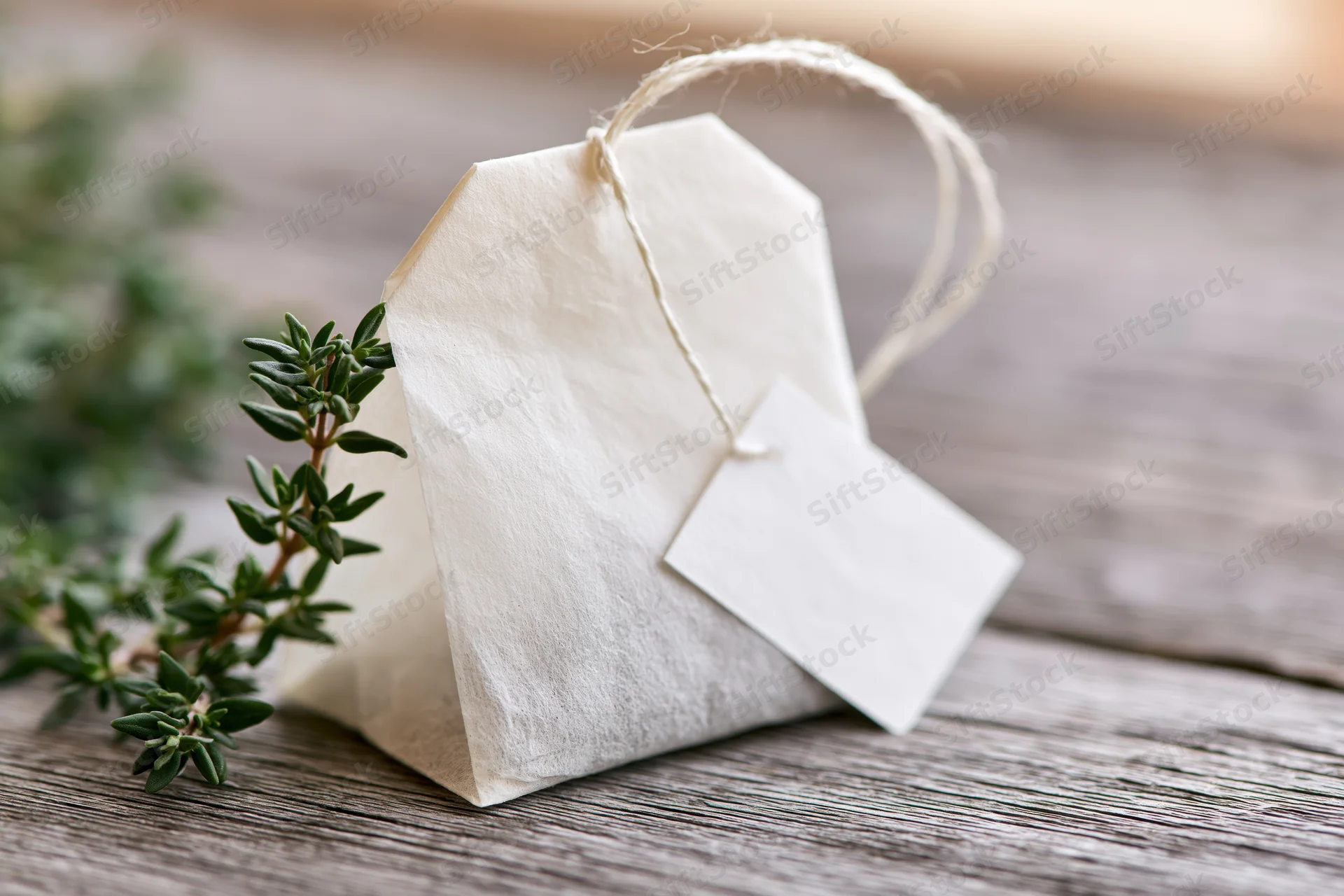 White paper tea bag with string tag and green herb sprig on wooden surface