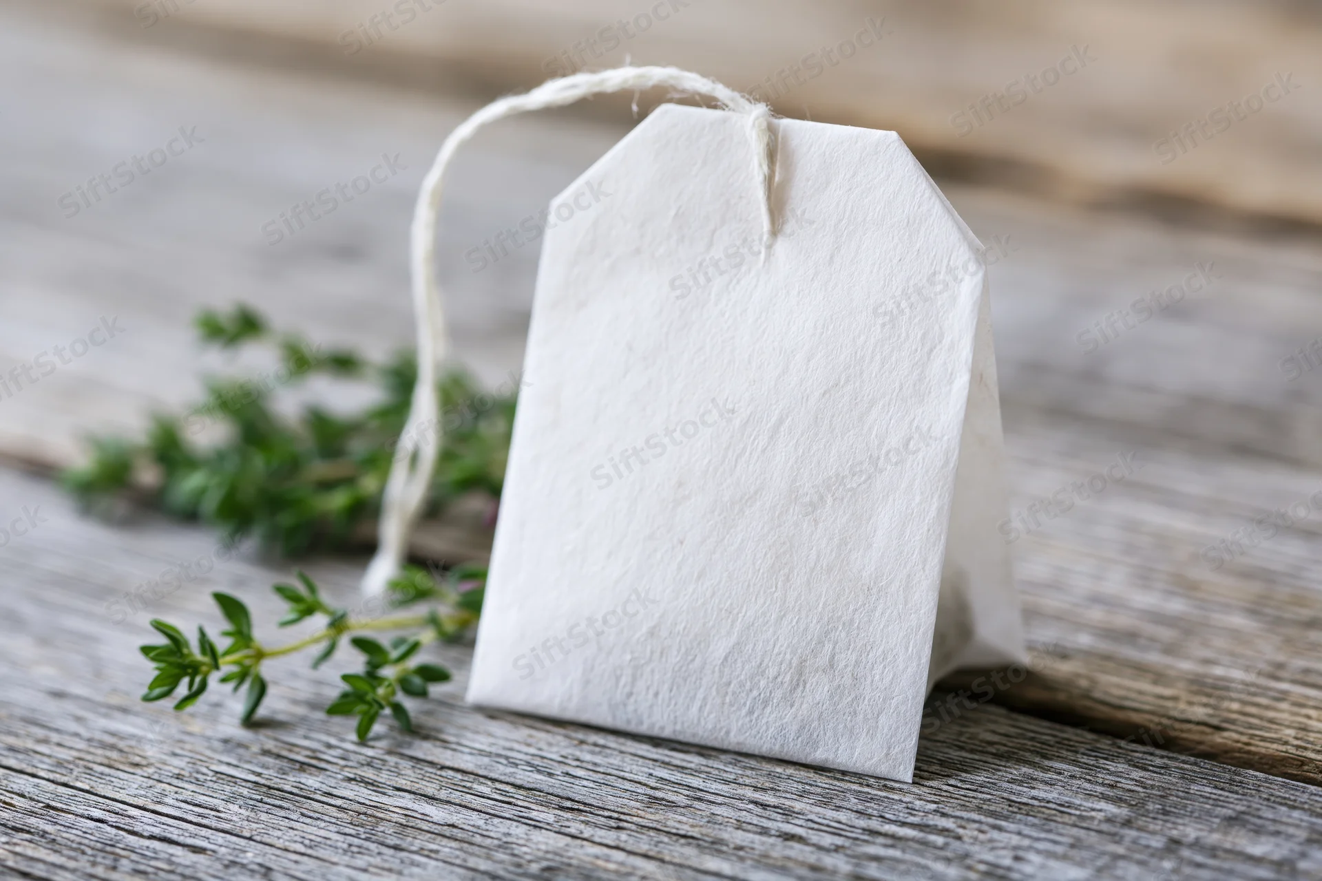 White paper tea bag with string tag resting on wooden surface beside fresh thyme sprig
