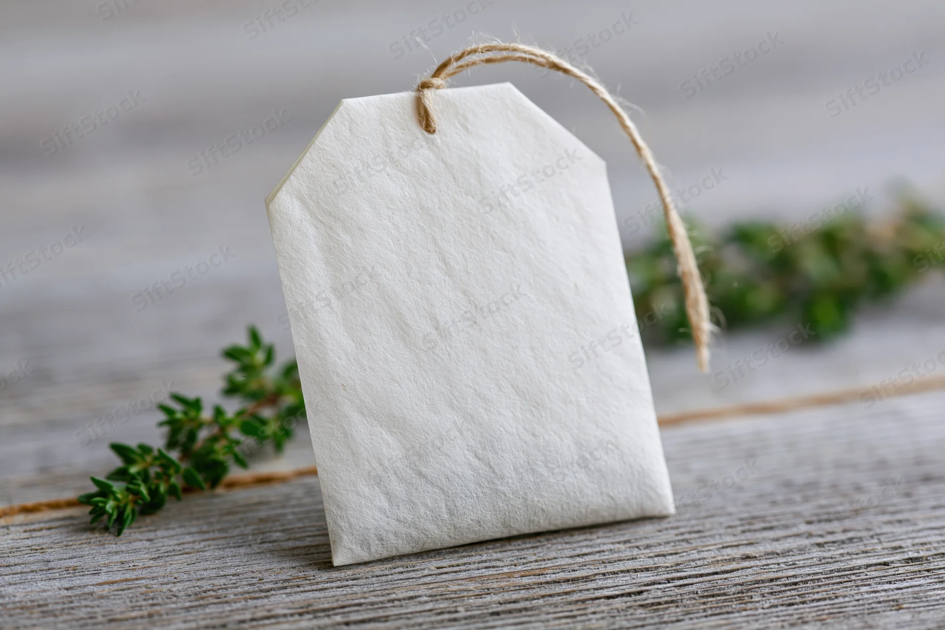 White paper tag with string resting on wooden surface beside green herbs