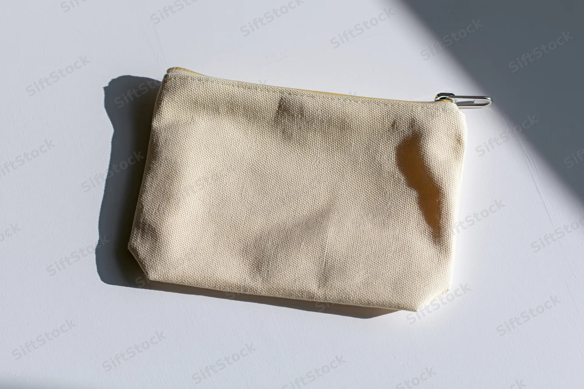 Small blank canvas zip pouch lying flat on white surface