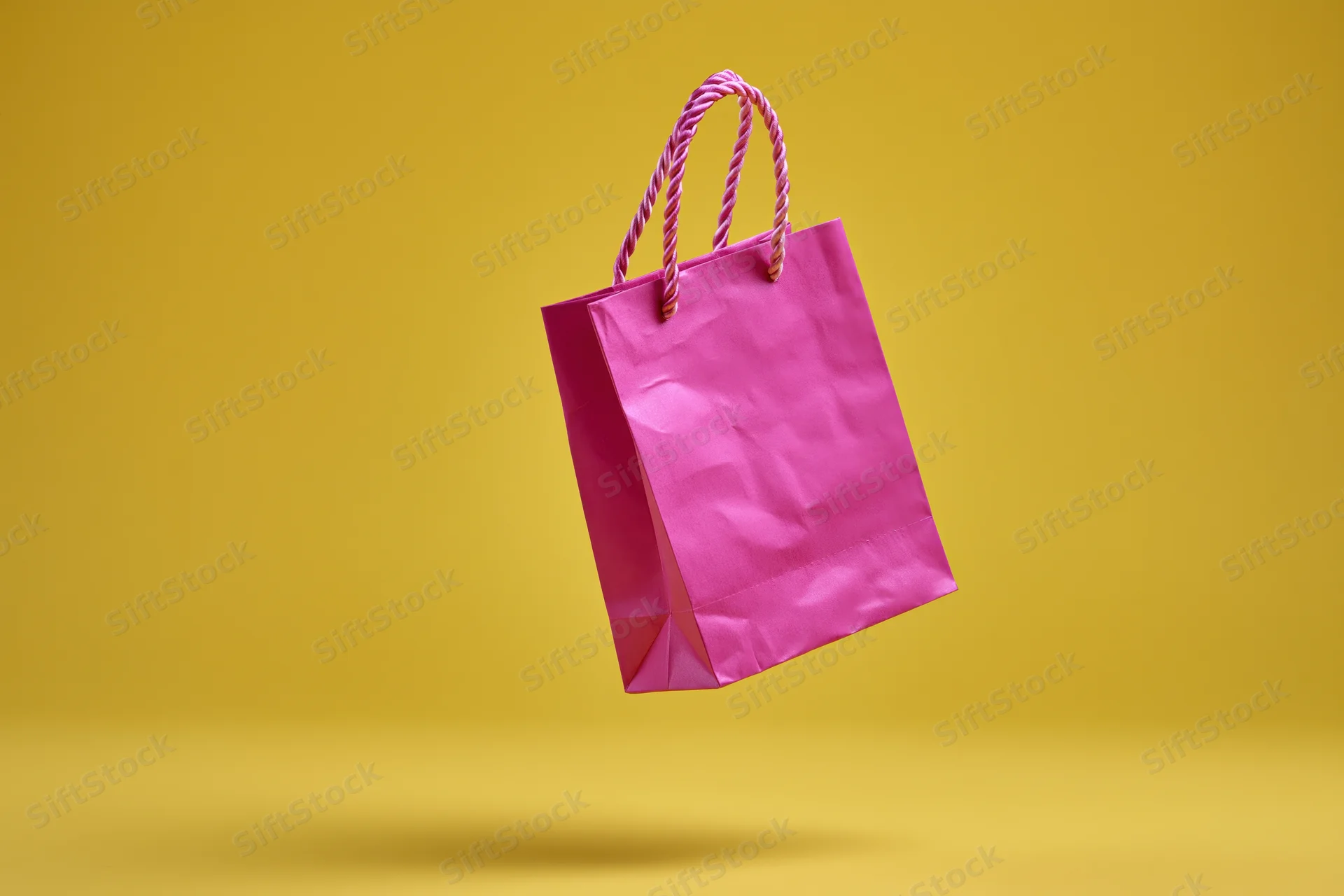 Pink paper shopping bag floating against yellow background