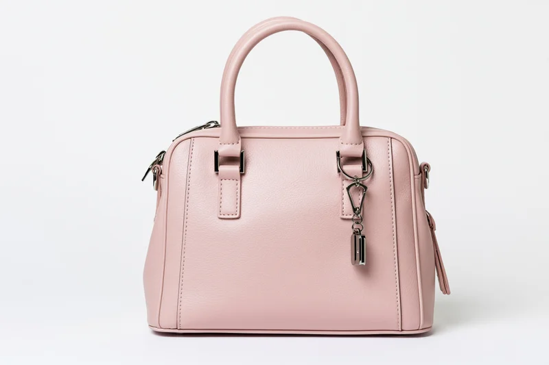 Small structured pink leather handbag with dual top handles and metal hardware on white background
