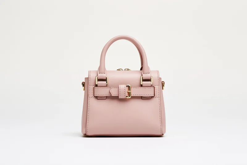 Small structured pink leather handbag with dual top handles and gold hardware on white background