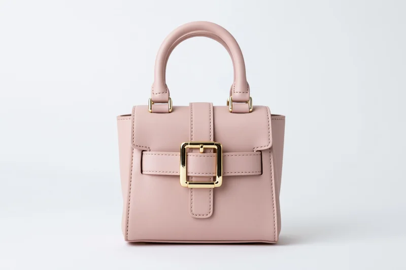 Small structured pink leather handbag with gold buckle and dual top handles on white background