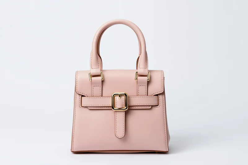 Small structured pink leather handbag with dual top handles and gold hardware on white background