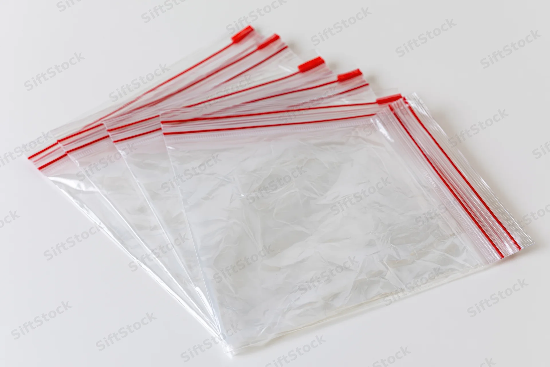 Fanned stack of clear resealable zip-lock plastic bags on white surface