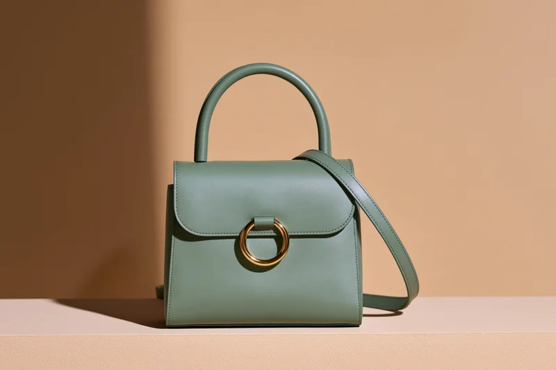 Sage green leather handbag standing upright on a beige surface with soft lighting and copyspace