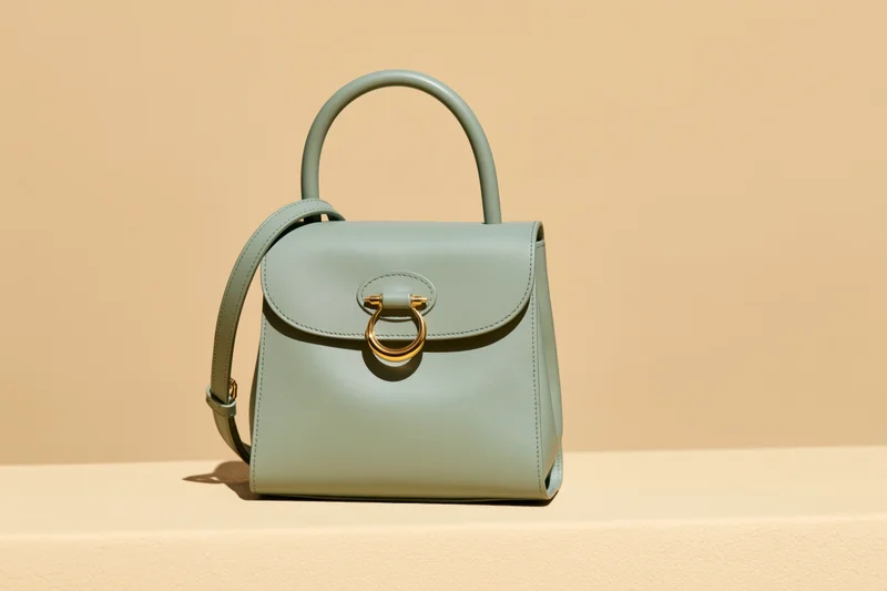 Sage green leather handbag with gold hardware sitting upright on a beige surface
