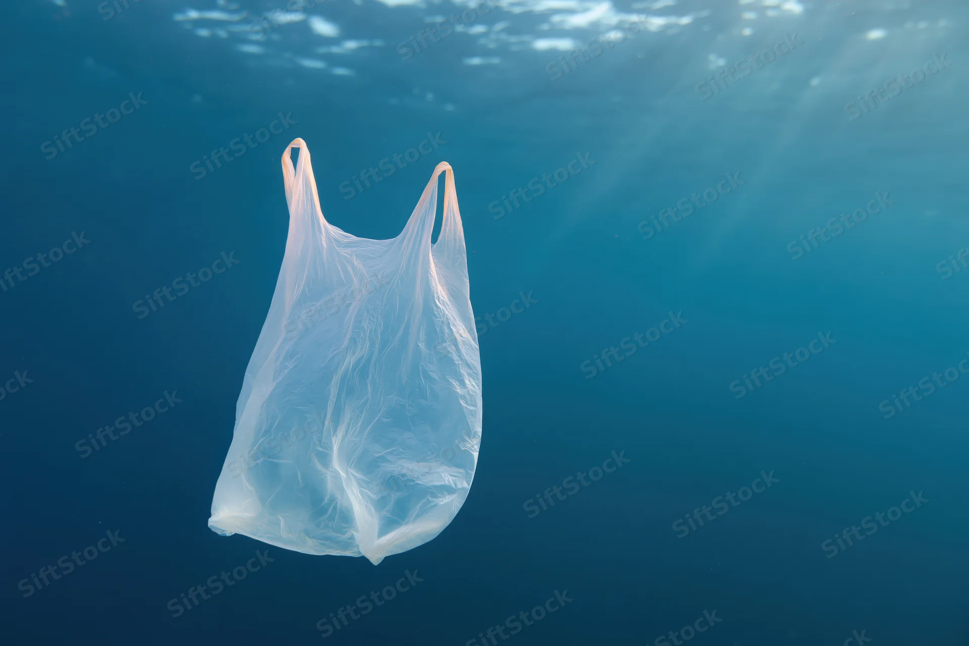Translucent white plastic bag drifting underwater in deep blue ocean with sunlight rays filtering through water