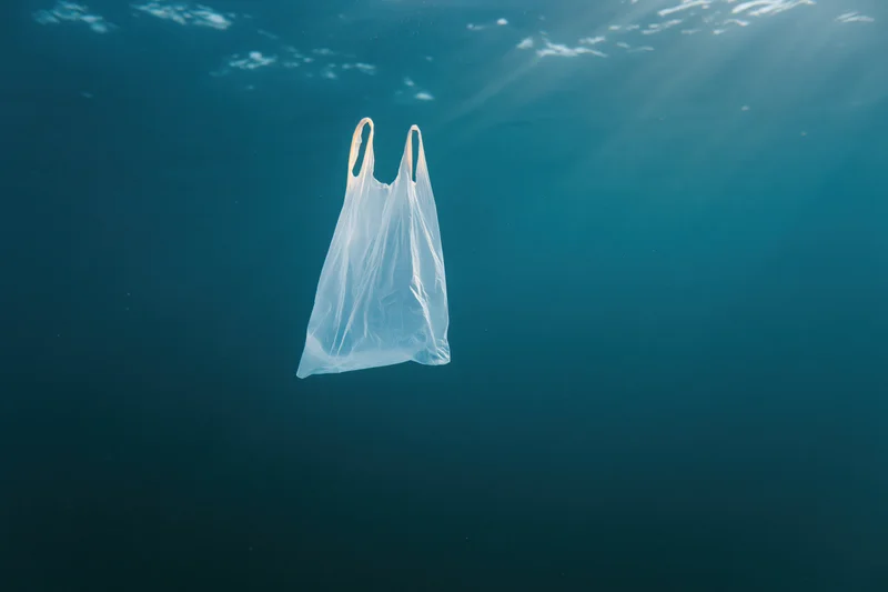 Translucent white plastic bag floating underwater in deep blue ocean with sunlight rays filtering through surface