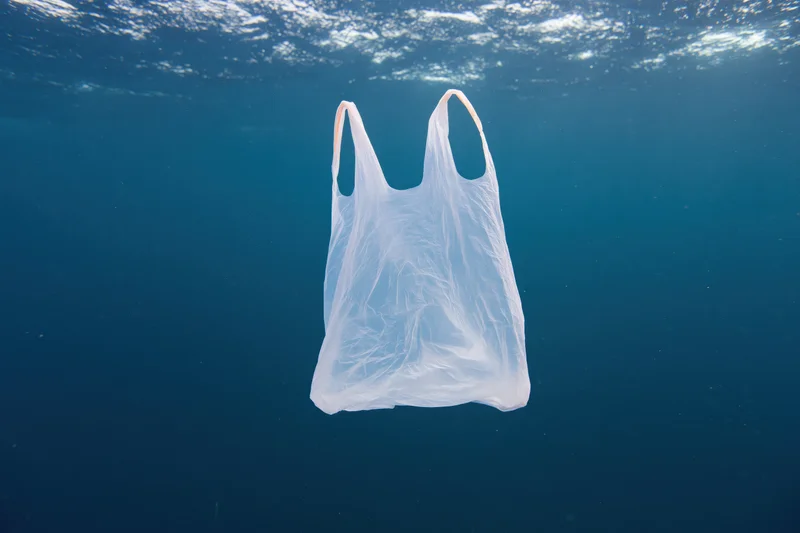 Translucent white plastic bag floating suspended in deep blue ocean water beneath sunlit surface