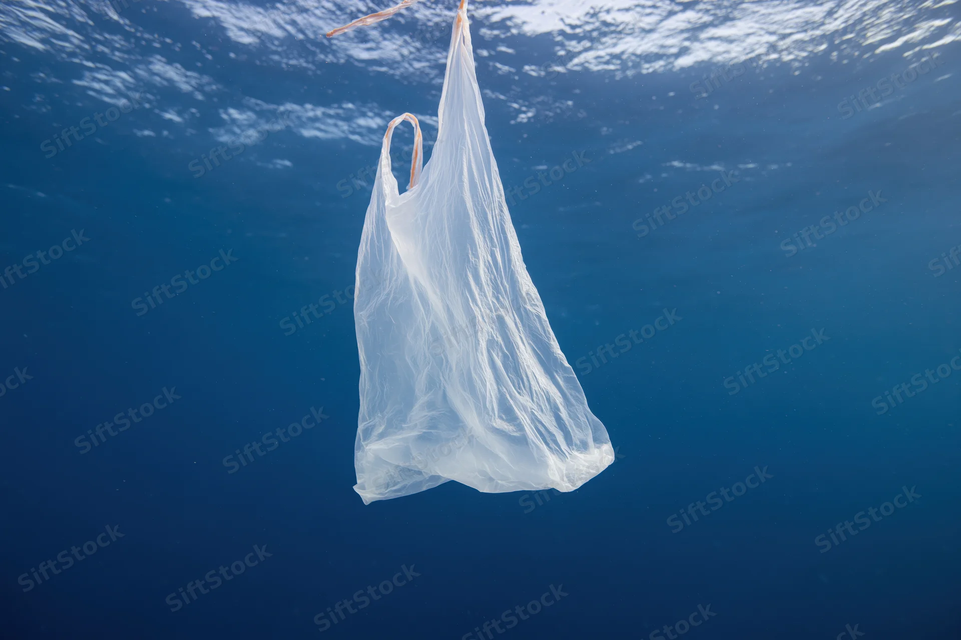 Translucent white plastic bag floating suspended in deep blue ocean water under sunlight
