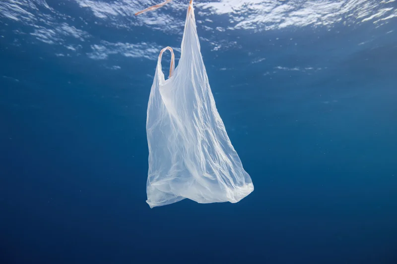 Translucent white plastic bag floating suspended in deep blue ocean water under sunlight