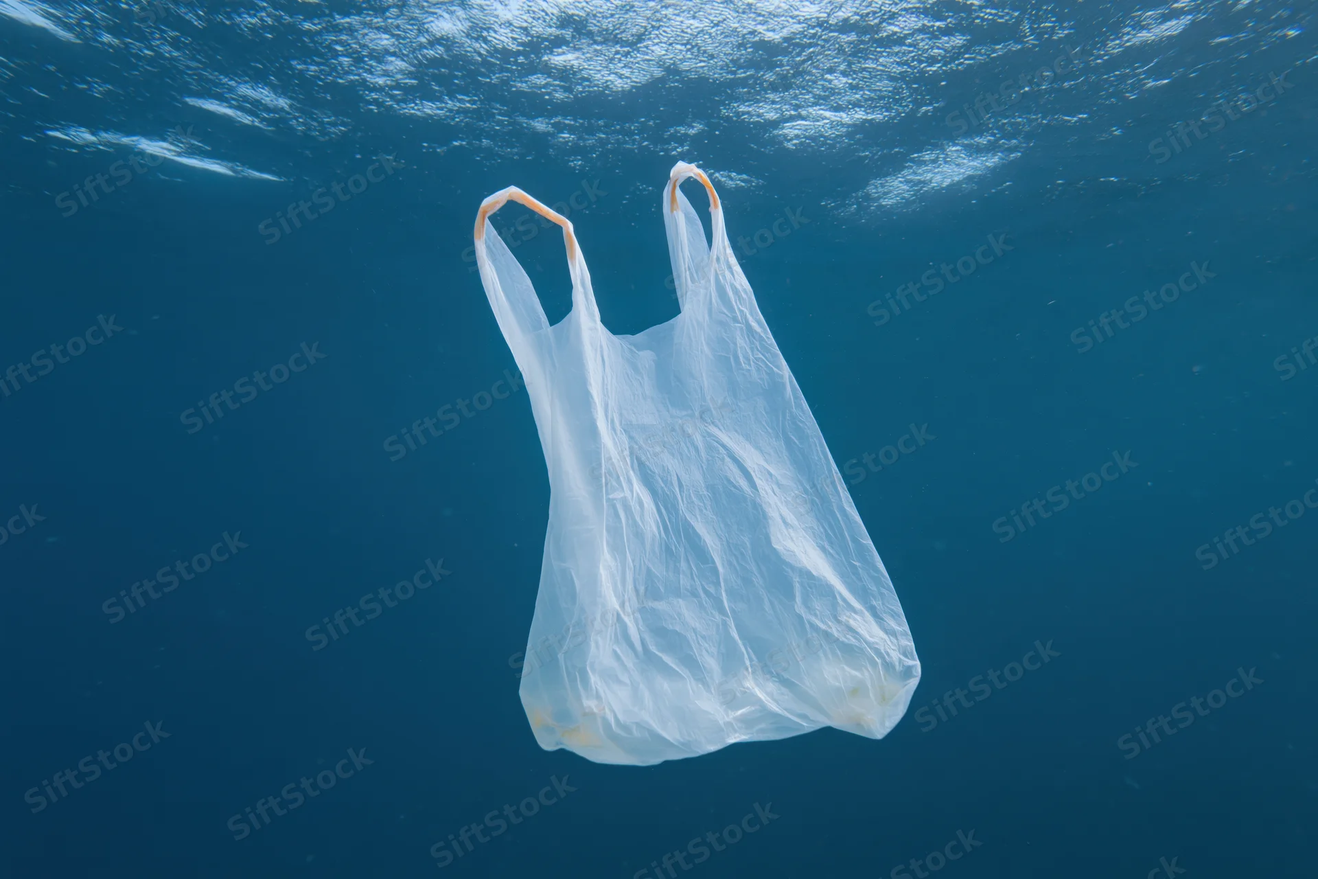 Translucent white plastic bag floating suspended in deep blue ocean water under sunlight