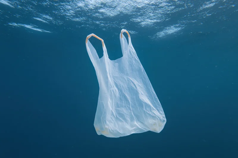 Translucent white plastic bag floating suspended in deep blue ocean water under sunlight