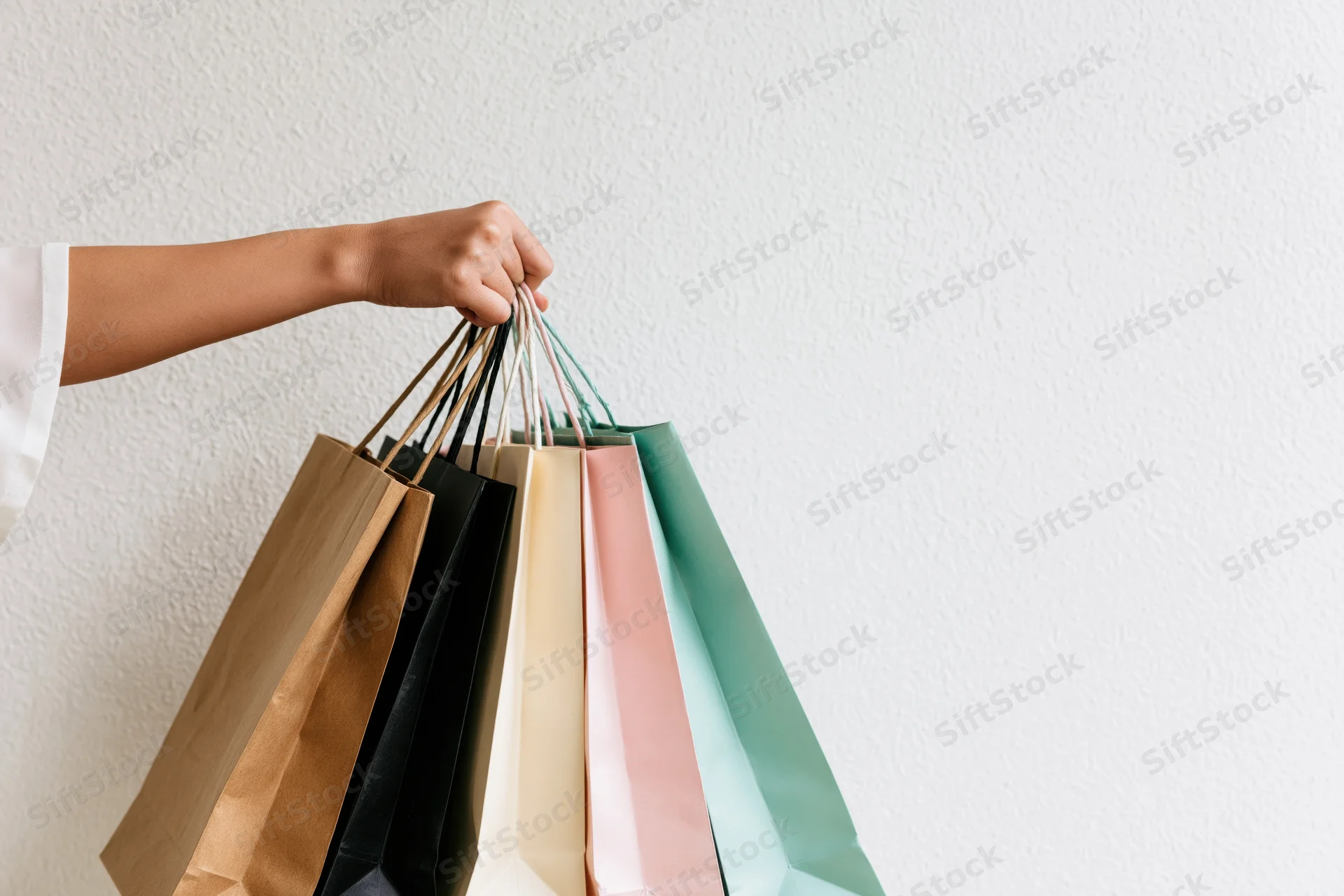 Woman’s hand holding multiple colorful shopping bags against a white textured wall