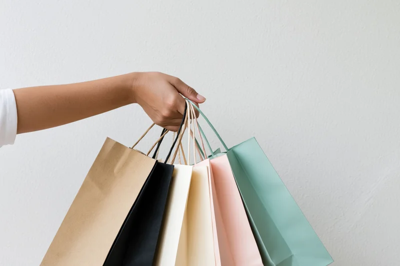 Woman’s hand holding multiple colorful shopping bags against a plain white background