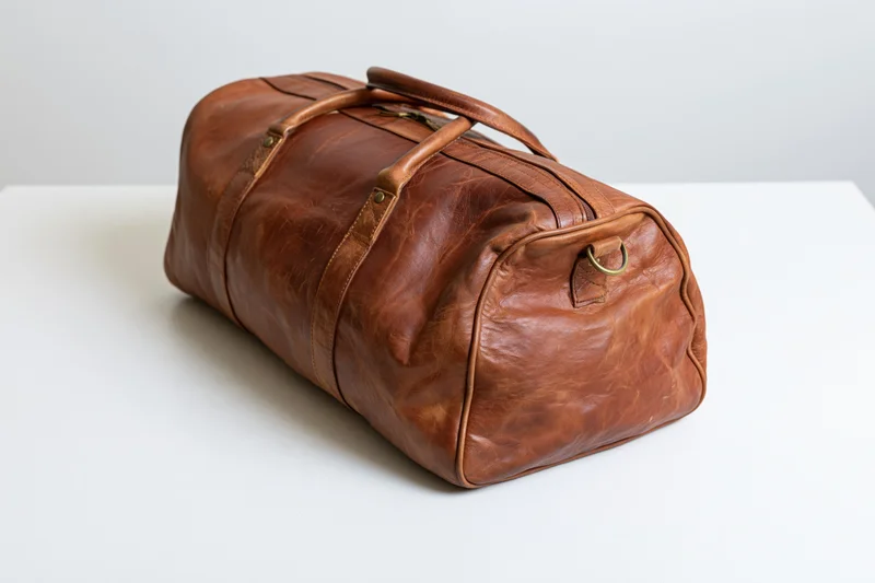 Brown leather duffle bag resting on white surface