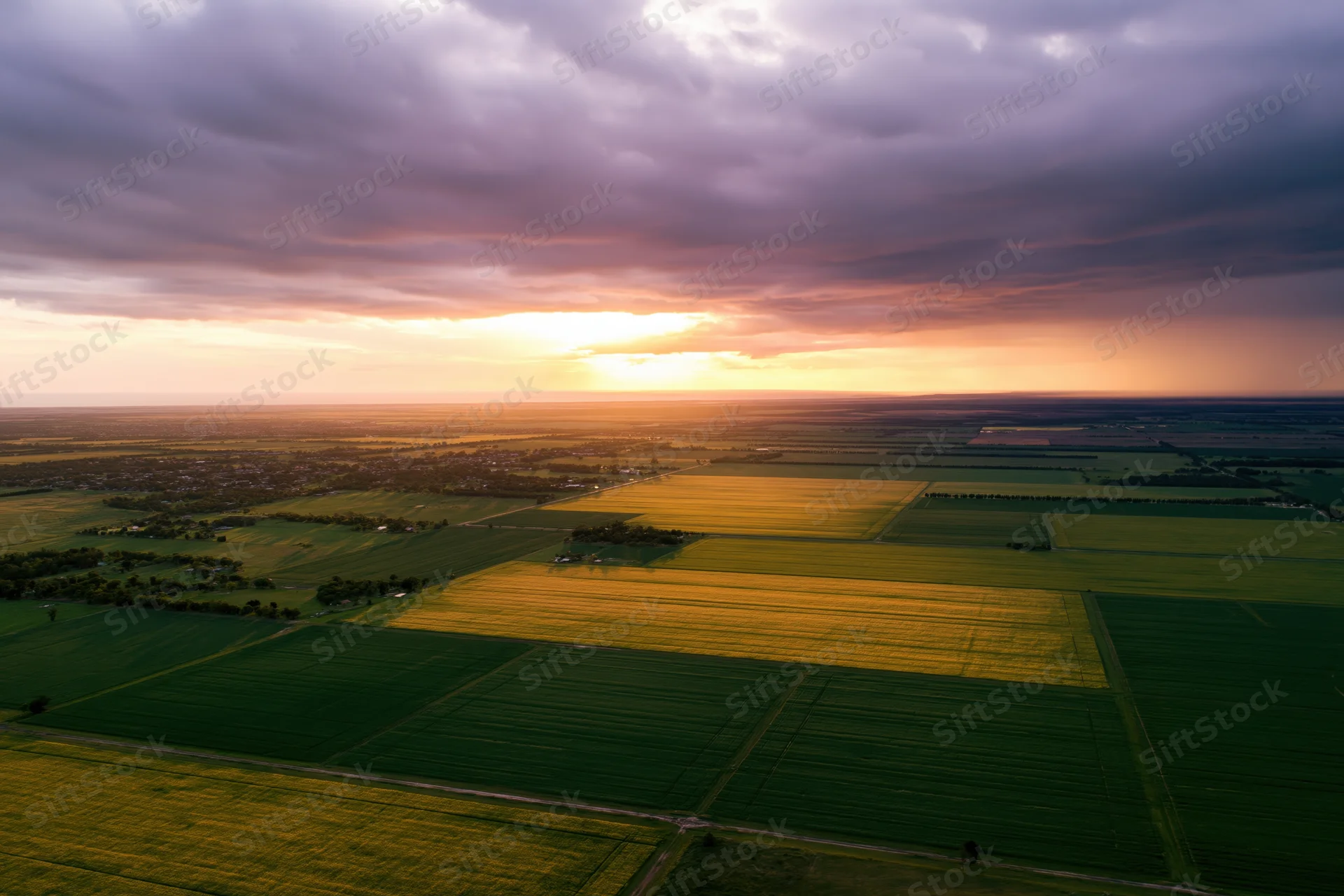 Aerial drone view of patchwork farmland at sunset with golden light over green and yellow fields