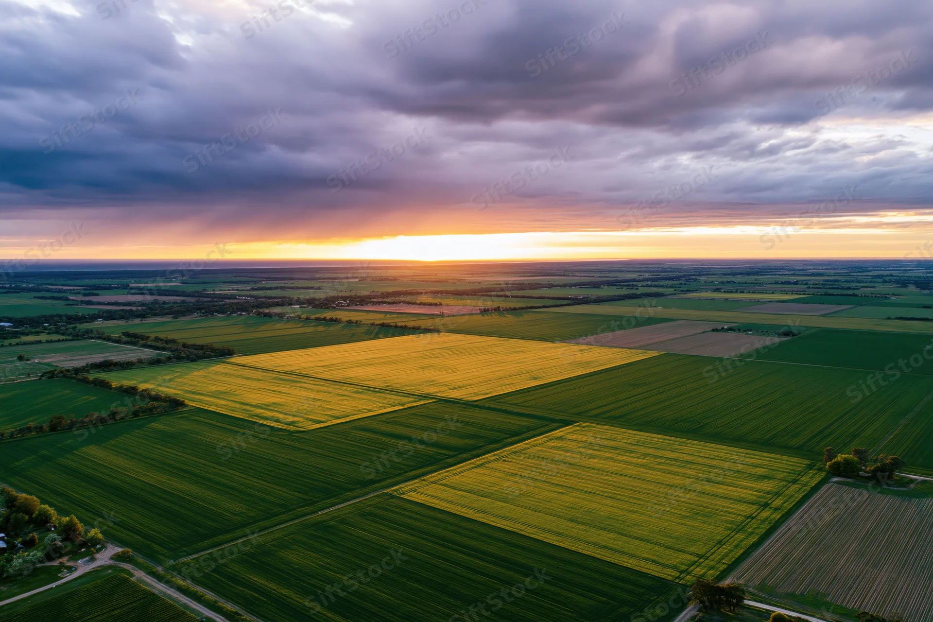 Aerial view of patchwork farmland at sunset with golden and green fields under cloudy sky